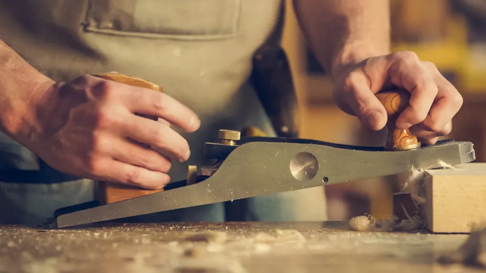 Mains de menuisier rabotant une pièce de bois